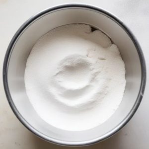 This image shows the process of mixing powdered sugar and vanilla essence together in a bowl for making the pineapple cake frosting.